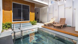 A modern outdoor pool area with a wooden deck, two lounge chairs, and a glass-enclosed room with a sliding door. - Modern Pool Home in Coco · Walk to Beach and Town (Playa del Coco)