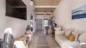 A modern living room with a sofa, a TV, a fan, and a kitchen in the background. - Modern Pool Home in Coco · Walk to Beach and Town (Playa del Coco)