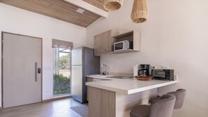 A modern kitchen with a central island, bar stools, a microwave, a coffee maker, and a refrigerator. - Modern Pool Home in Coco · Walk to Beach and Town (Playa del Coco)