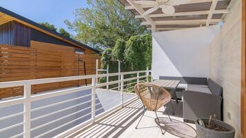 A balcony with a wooden floor, a white railing, a wicker chair, a table, and a potted plant.