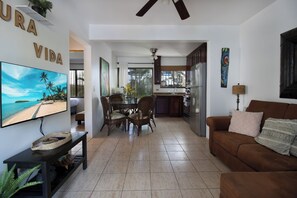 A living room with a TV, a dining area with chairs, a kitchen with cabinets, and a ceiling fan. - Beach Escape in Las Palmas•Pool•Walk to Everything (Playa del Coco)