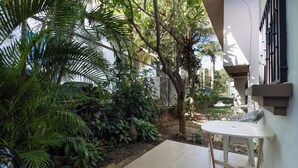 Uma área de pátio com mesa e cadeiras, cercada por vegetação exuberante e um muro de pedra.