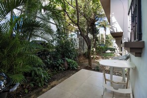 A patio area with a table and chairs, surrounded by lush greenery and a stone wall. - Beach Escape in Las Palmas•Pool•Walk to Everything (Playa del Coco)