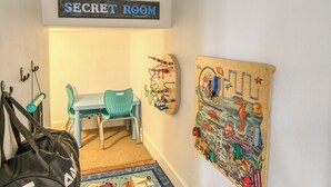 Una stanza con un cartello che riporta la scritta 'SECRET ROOM' sopra una scrivania e una sedia, un tappeto colorato e una decorazione a parete.