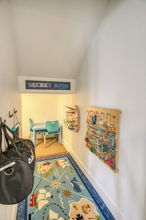 Um quarto com uma placa que diz 'SECRET ROOM' acima de uma escrivaninha e uma cadeira, um tapete colorido e uma decoração na parede.