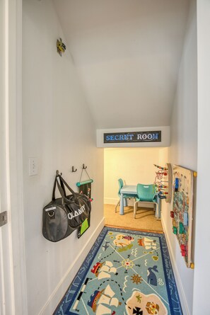 A hallway with a sign reading 'SECRET ROOM' above a door, a child's play area with a mat, and a wall-mounted bag.