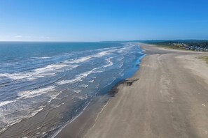 Una playa con olas, una orilla arenosa y una vista distante de casas.