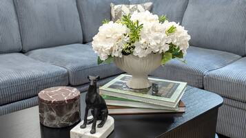 A grey sofa, a white vase with flowers, a book, a marble container, and a black statue on a black table.