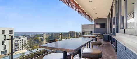 Une terrasse extérieure moderne, dotée d’une longue table et de sièges, offrant une vue sur le paysage urbain.