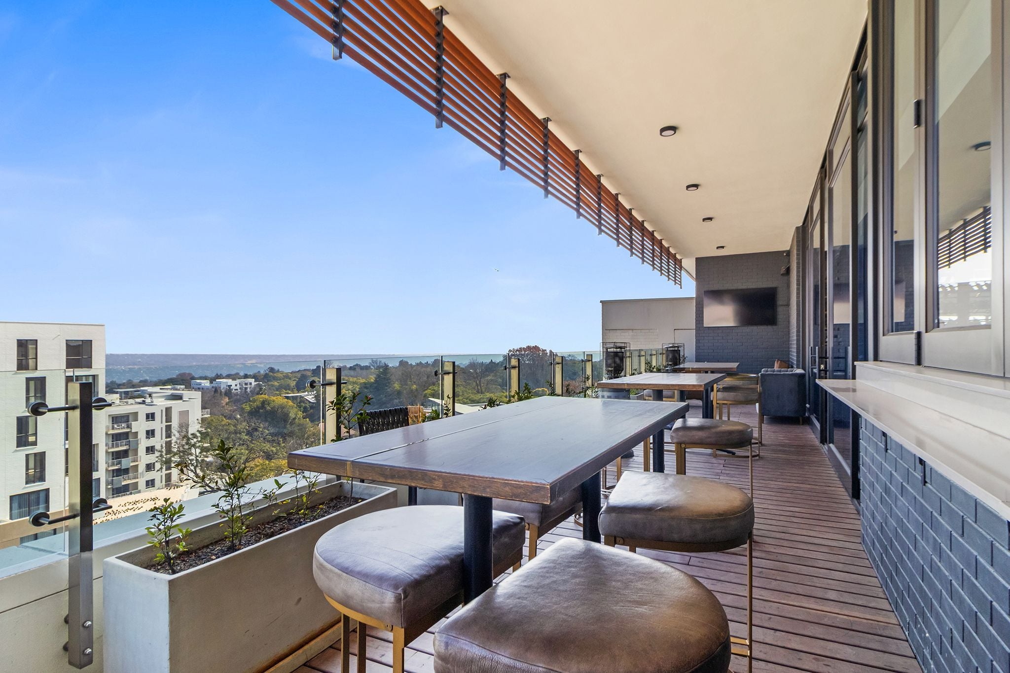 Une terrasse extérieure moderne, dotée d’une longue table et de sièges, offrant une vue sur le paysage urbain.