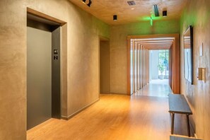 Ein moderner Flur mit Holzboden, einer Bank und einer Tür mit Aufzugssymbol.