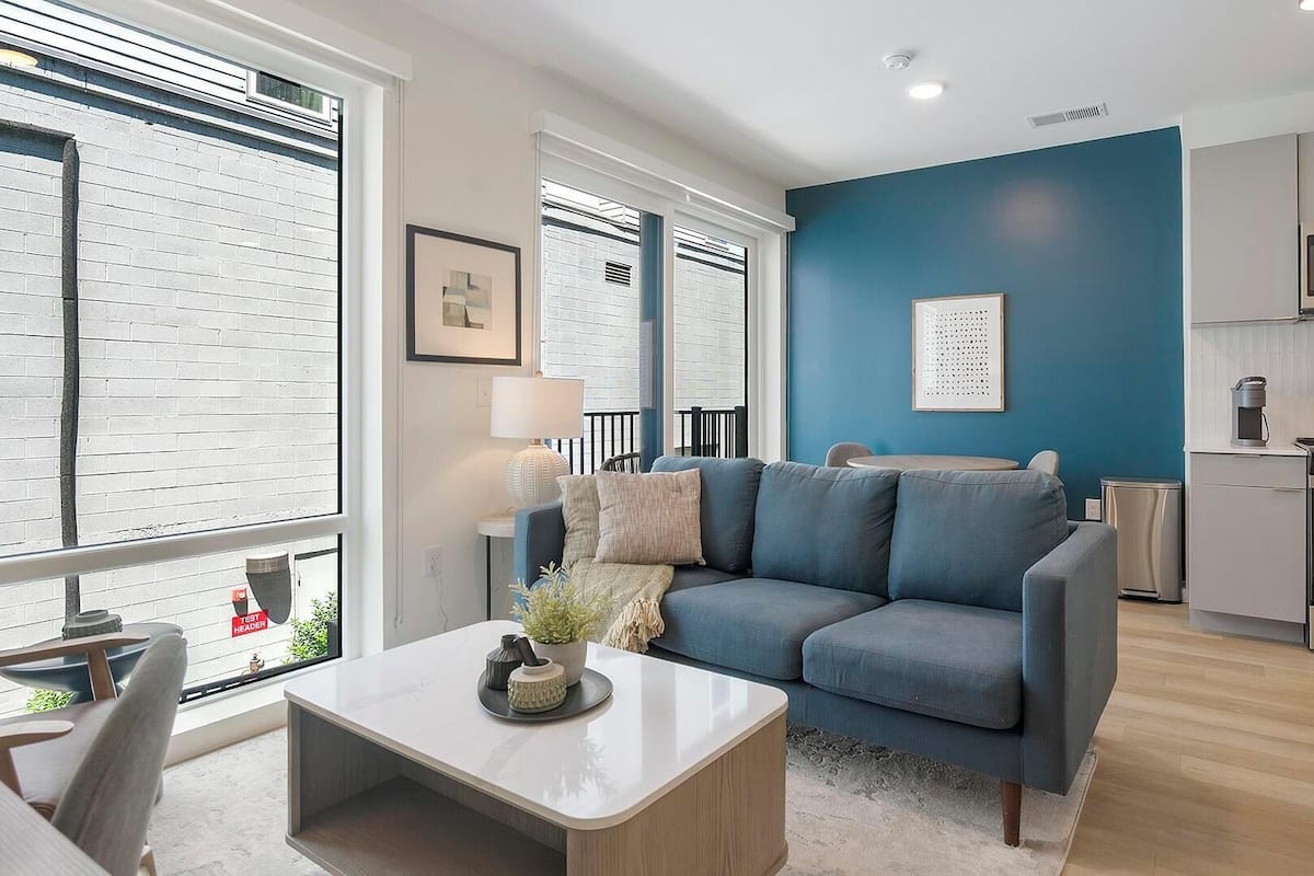 A modern living room with a blue sofa, a coffee table, and a view of the kitchen.