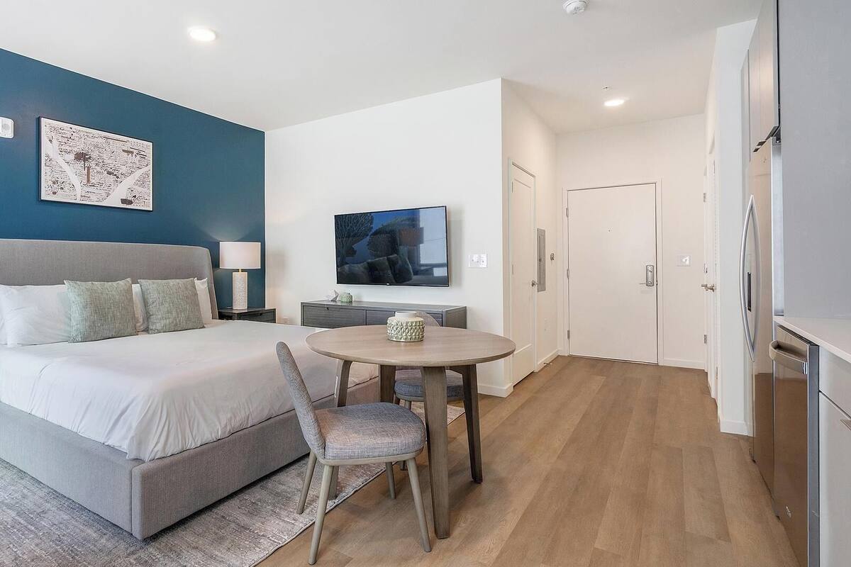 A modern hotel room with a large bed, a dining table, and a TV.