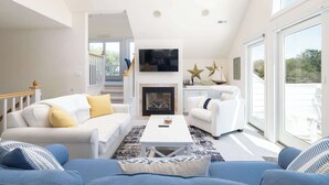 A spacious living room with a fireplace, white sofas, a coffee table, and large windows. - Currituck Club Retreat with Pool, Spa & Golf Views (Corolla)