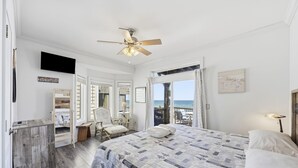 Une chambre à coucher avec un lit, un ventilateur de plafond, une télévision, une armoire en bois, une chaise, un bureau et une vue sur l’océan.