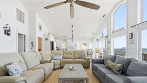 Un salon spacieux doté d’un ventilateur de plafond, de grandes fenêtres et offrant une vue sur l’océan.
