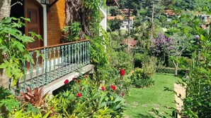 A wooden house with a balcony, surrounded by lush greenery and a garden. - Casarão Hortência (Teresópolis)
