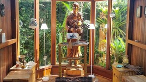 A wooden interior with a statue, wooden tables, and a view of greenery outside. - Casarão Hortência (Teresópolis)