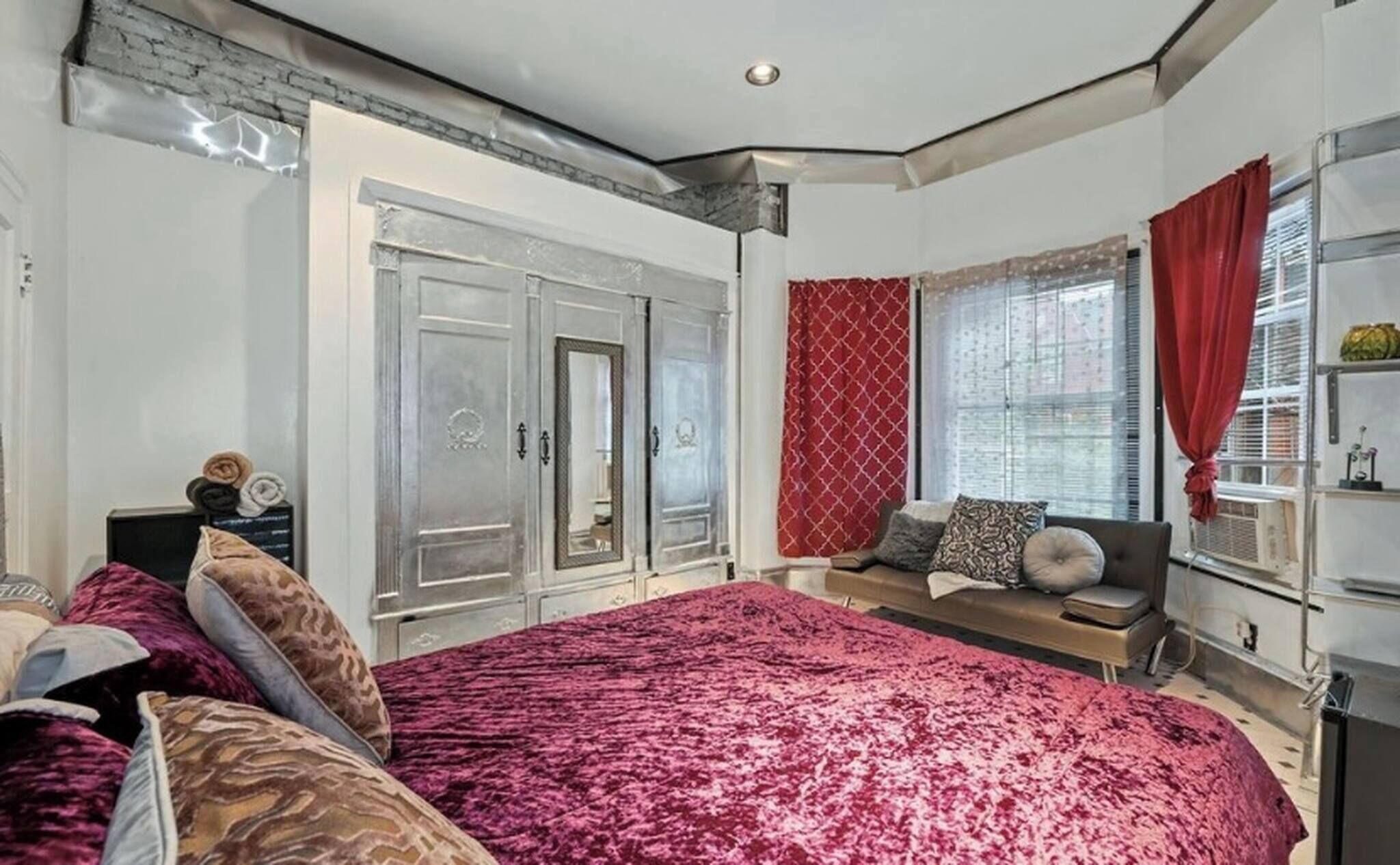 A bedroom with a large bed, a wardrobe, a seating area with a bench, and a window with curtains.