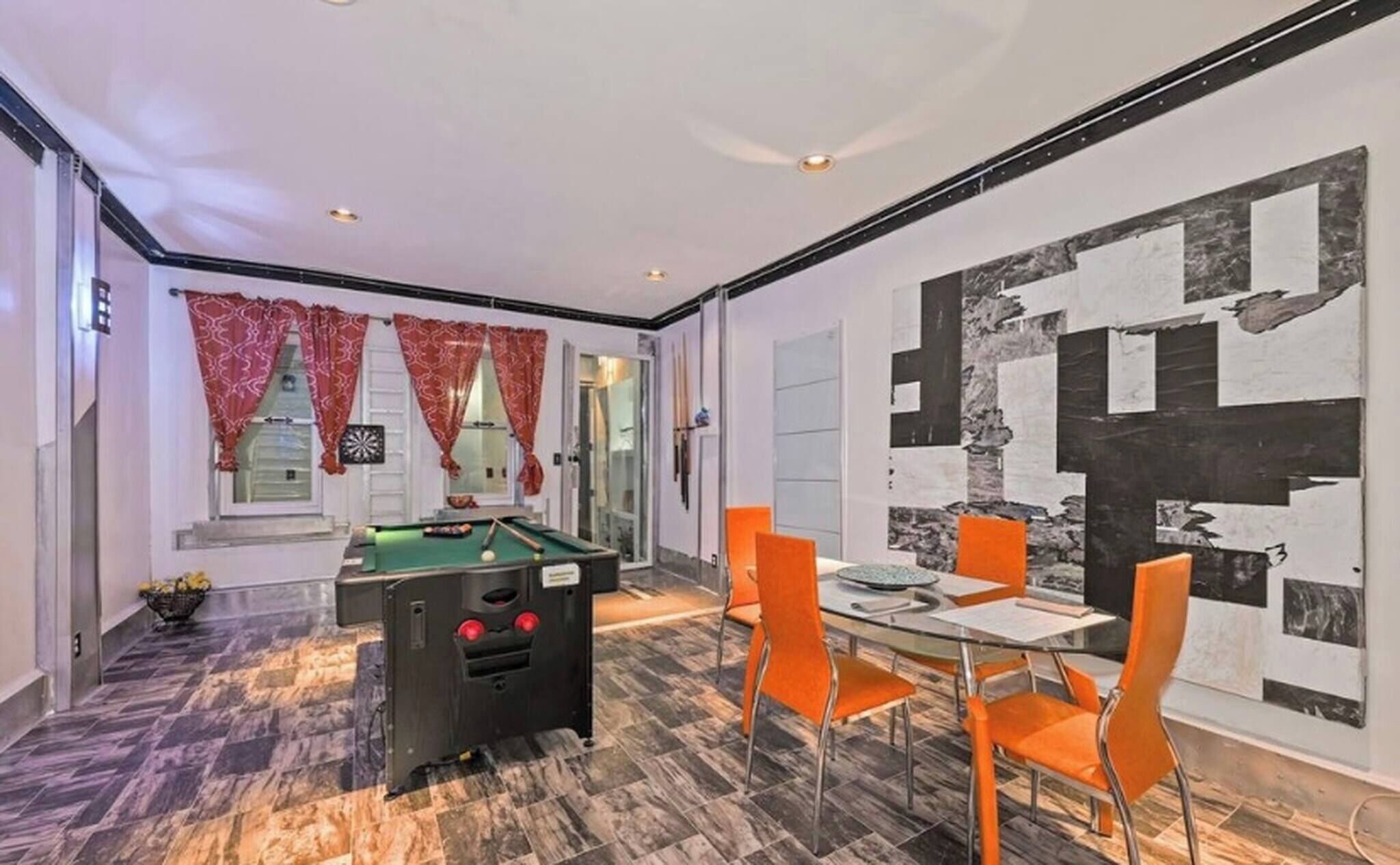 A room with a pool table, a dining table with chairs, and a large abstract painting on the wall.