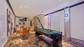 A pool table in a room with a marble floor, a staircase, and a dining area with chairs.