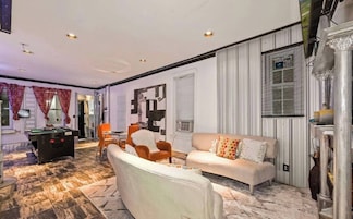 Un salón amplio con sofá, sillones, mesa de billar y un adornado en la pared.