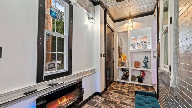 A hallway with a fireplace, a shelf with decorative items, and a door leading to another room.