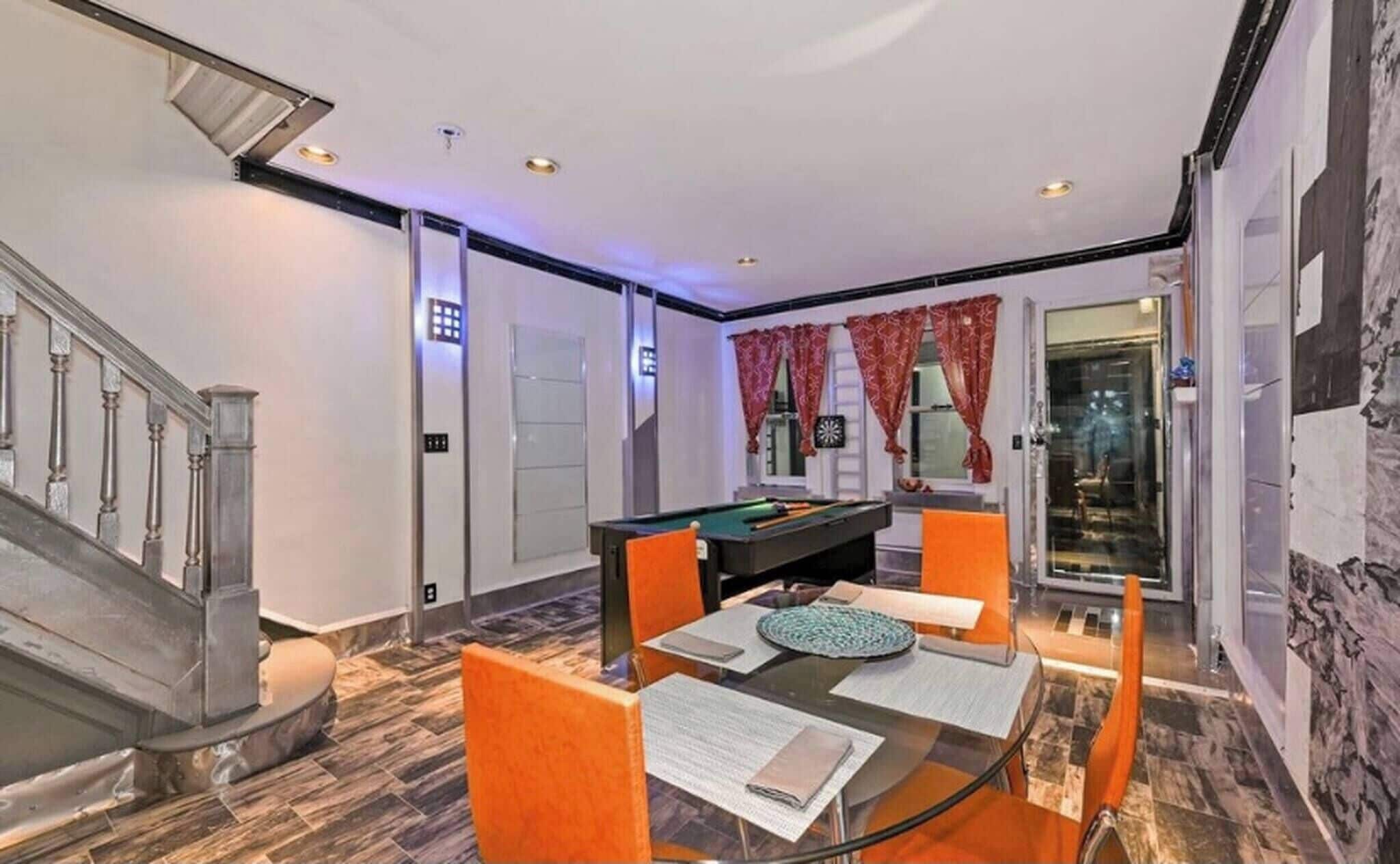 A modern interior with a pool table, dining area, and a staircase.
