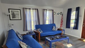 A living room with two blue sofas, a coffee table, and striped curtains. - Tiny Home Walking Distance to the Beach (Port O`Connor)