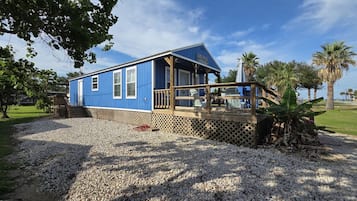 A blue building with a wooden deck, surrounded by gravel and palm trees.