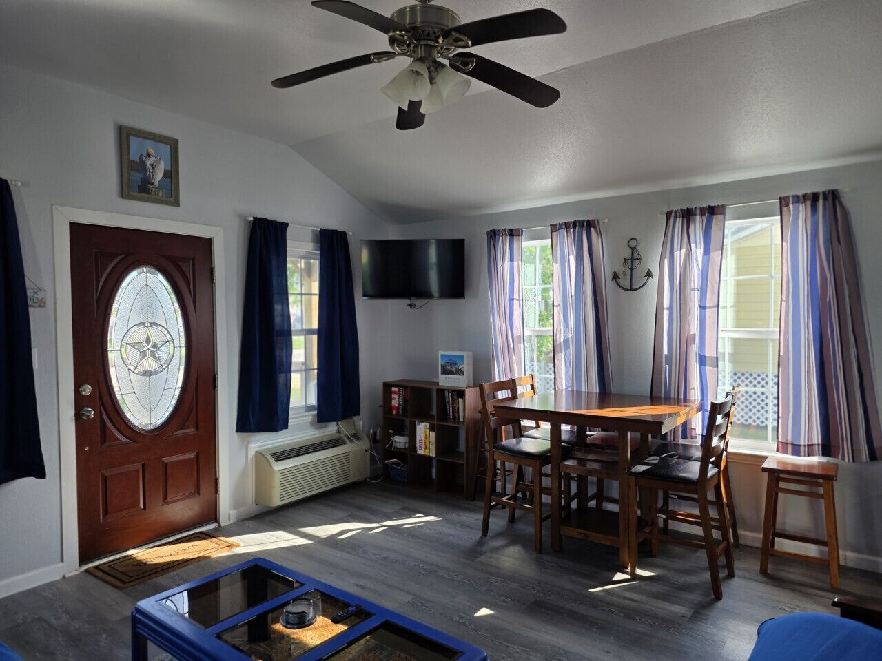 A living room with a wooden table, chairs, a ceiling fan, a TV, and a door with a glass window.