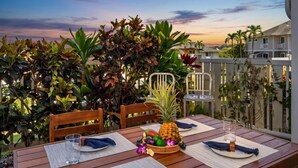 Une table en bois, dressée pour le repas, avec des chaises, un ananas en guise de décoration centrale et une vue sur un quartier résidentiel bordé de palmiers.