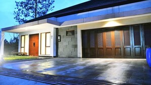 A modern building with a large garage door, a wooden door, and a paved driveway. - Cempaka 2 Villa Dago Private Pool (Bandung)