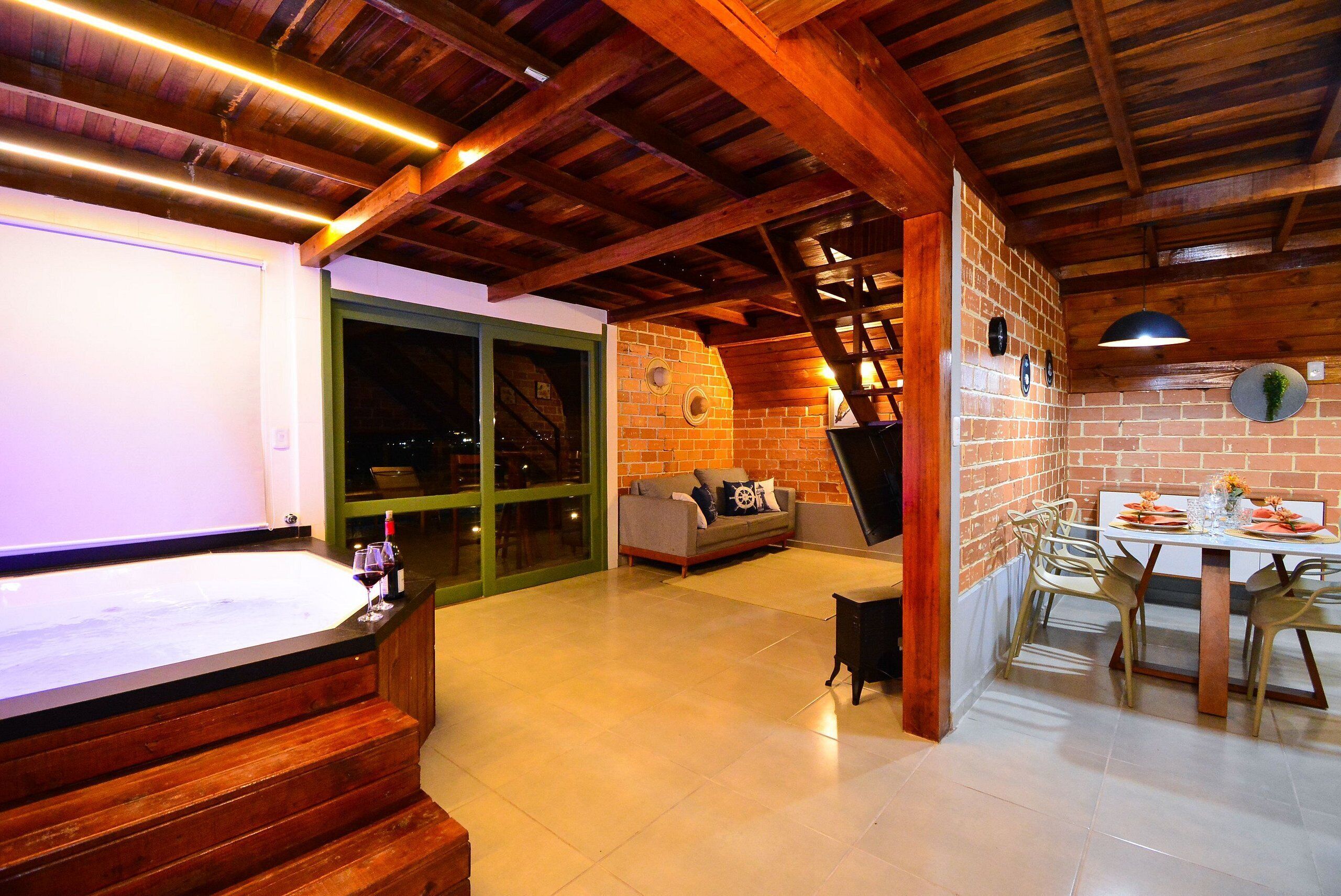 Una habitación espaciosa con techo de madera, pared de ladrillo, zona de comedor con mesa y sillas, y un ventanal grande.