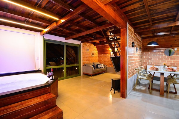 A spacious room with a wooden ceiling, a brick wall, a dining area with a table and chairs, and a large window.