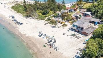 An aerial view of a coastal area with a beach, parked cars, and buildings.