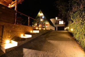 Une vue nocturne d’un bâtiment à l’extérieur en bois, avec un escalier menant à un balcon du deuxième étage et une allée bien éclairée.