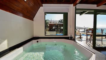 A hot tub in a room with a view of the sea and mountains.