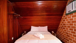 Uma cama de solteiro com roupa de cama branca, teto de madeira e parede de tijolos.