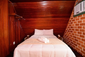 Un lit simple avec une literie blanche, un plafond en bois et un mur en briques.