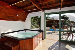 A wooden hot tub with a view of a pool and outdoor seating area. - Chalé com Jacuzzi e Vista Mar - PLH007 (Palhoça)