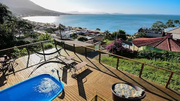 A wooden deck with a pool, outdoor furniture, and a view of the sea.