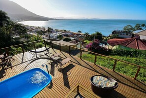 Una terraza de madera con piscina, mobiliario exterior y vista al mar.