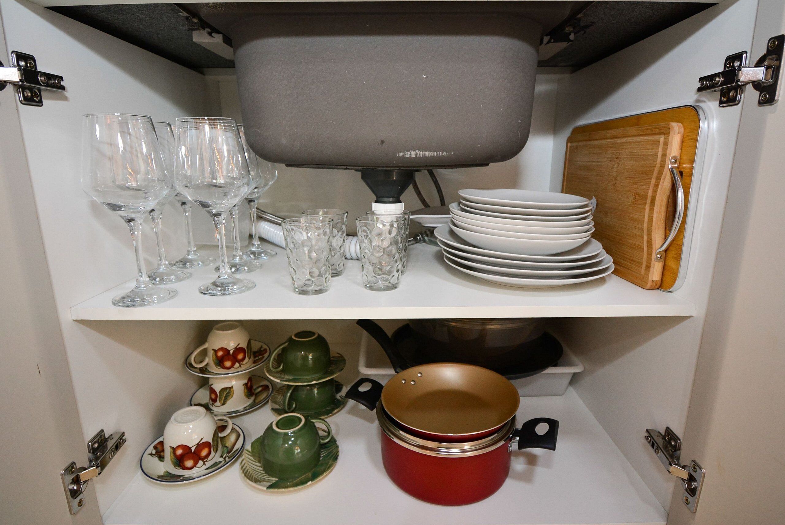A kitchen cabinet with wine glasses, plates, cups, and cookware.