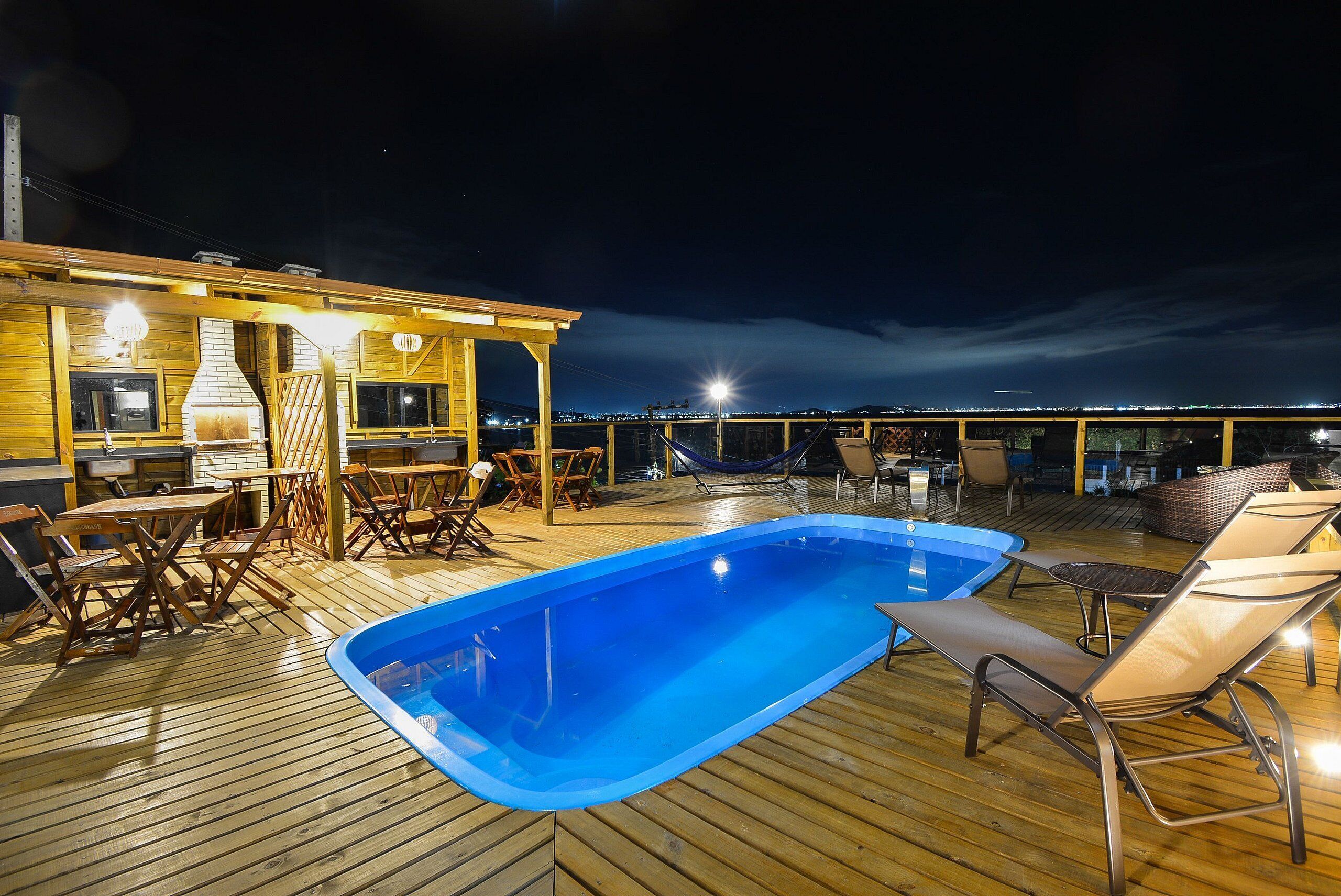 A wooden deck with a swimming pool, lounge chairs, and a barbecue area.