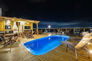 Une terrasse en bois avec une piscine, des chaises longues et un espace barbecue.