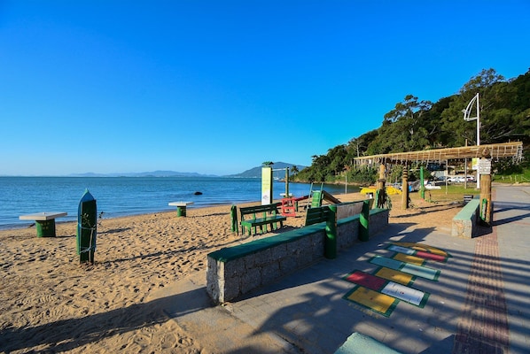 A beach with a bench, a covered area, and a view of the sea and mountains.