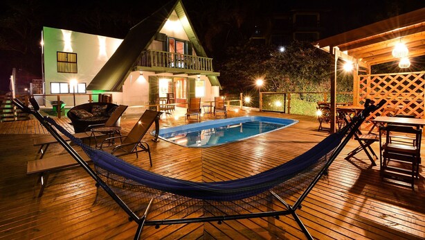 Um deck de madeira com uma rede, piscina e um edifício com varanda.