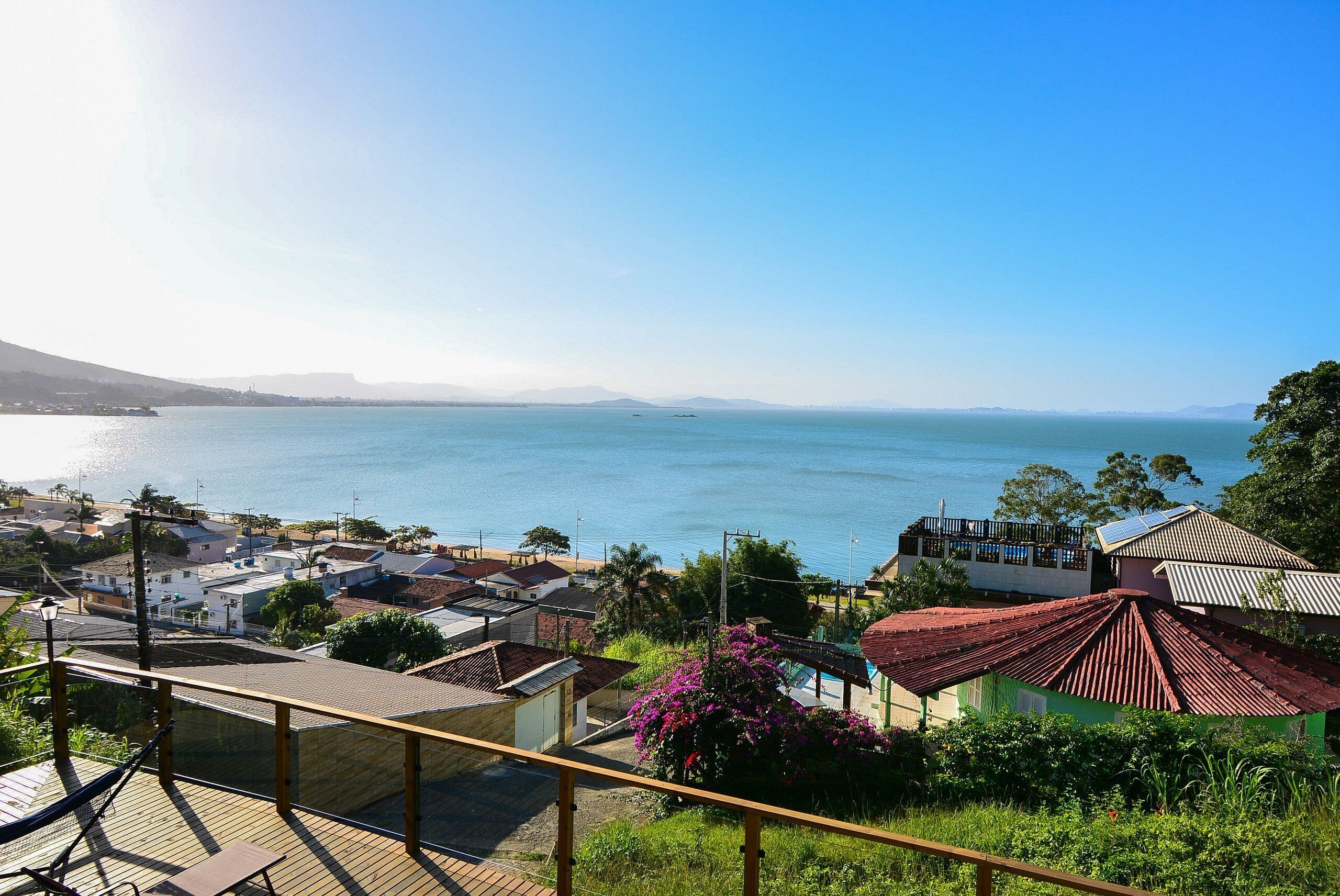 Vista costera con una terraza de madera, una hamaca y vistas al mar y montañas distantes.