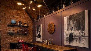 A bar area with a brick wall, shelves with bottles, a globe, and a painting of a woman.